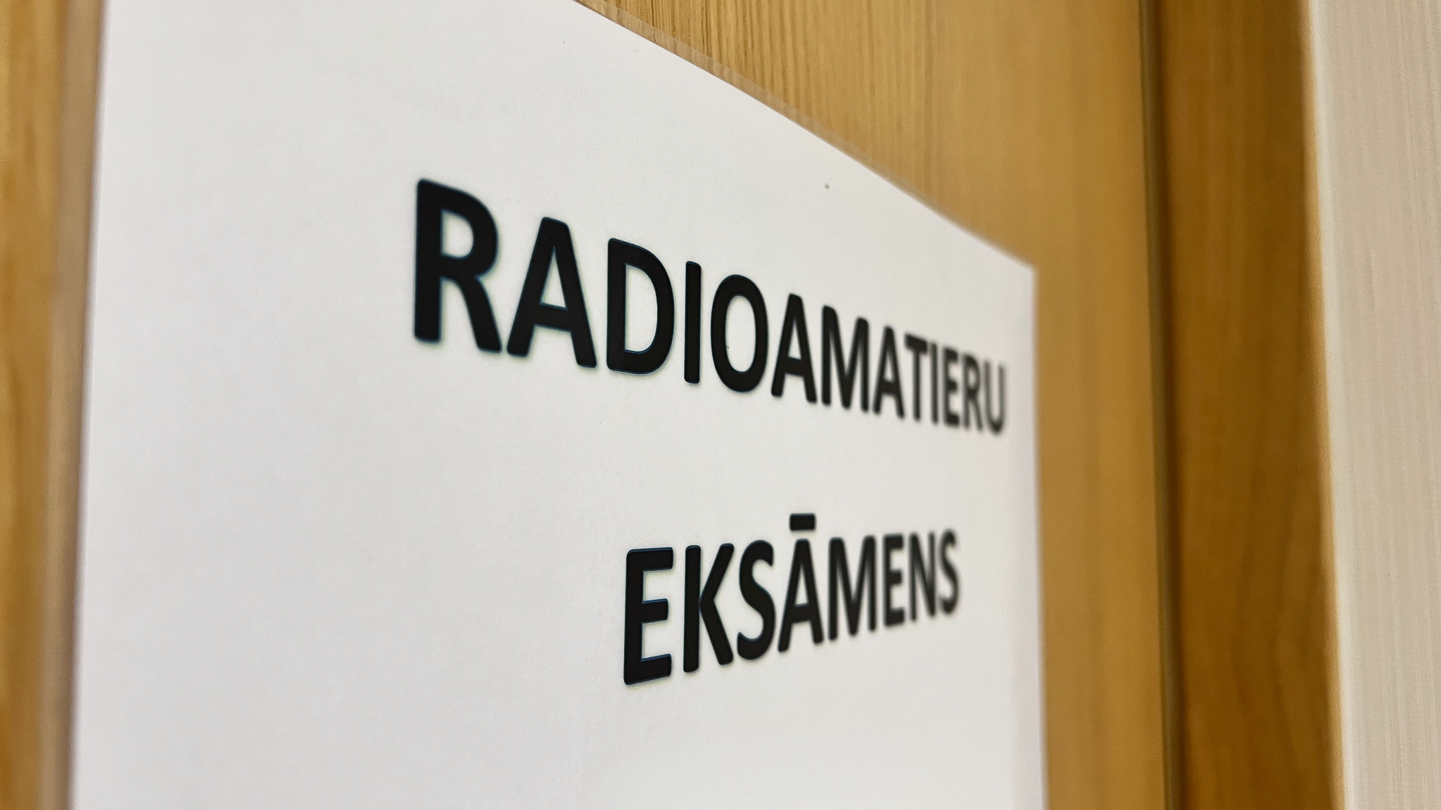 Uz durvīm uzlīmēta balta lapa, uz kuras rakstīts ''Radioamatieru eksāmens''