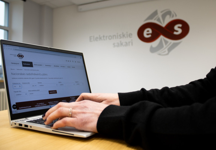 Persona izmanto datoru ar atvērtu Nacionālā radiofrekvenču plāna digitālo pārlūku, fonā redzams SIA "Elektroniskie sakari" logo