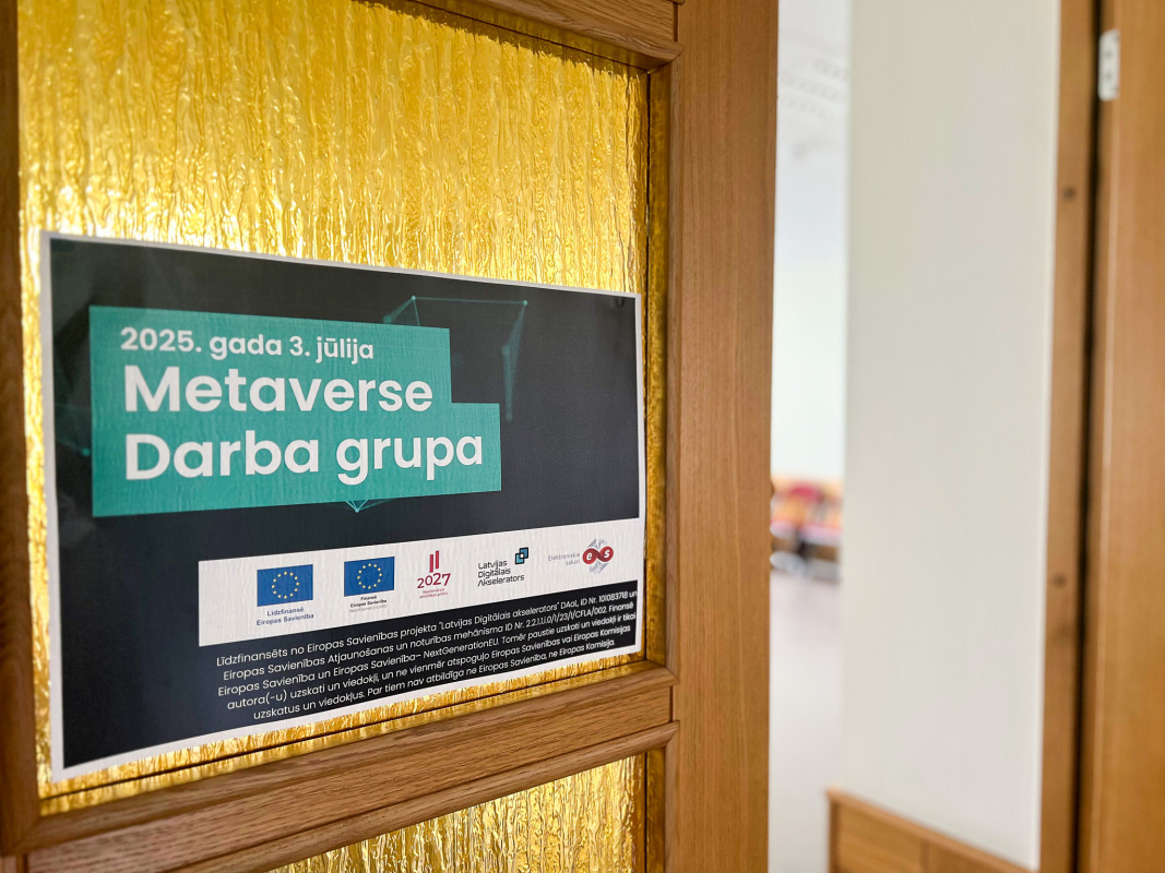 Attēlā redzama koka durvju daļa ar dzeltenu matētu stiklu, uz kuras piestiprināts plakāts ar uzrakstu “2025. gada 3. jūlija Metaverse Darba grupa”. Zem virsraksta redzami Eiropas Savienības, Latvijas Digitālās Akseleratora un SIA “Elektroniskie sakari” logotipi, kā arī projekta informācija. Fonā, caur atvērtām durvīm, redzama gaiša telpa ar koka apdari un mēbelēm.